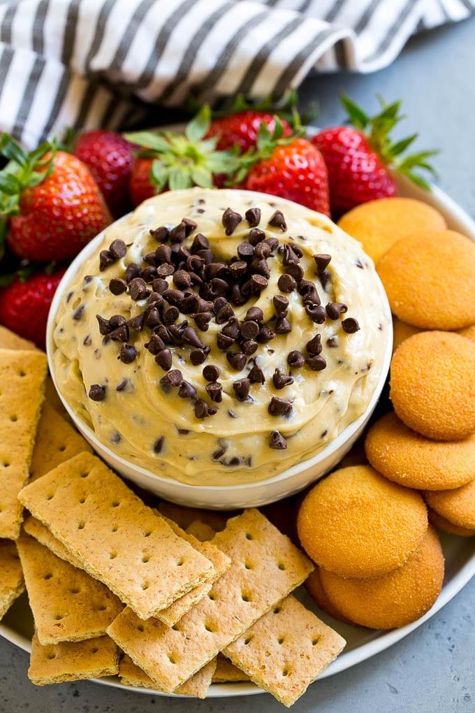 Cookie Dough Dip Rezept | Essbarer Cookie Dough | Schoko-Chip-Keks-Dip #cookies #dip #cookiedough #dessert #snack #ahurt Eine Schüssel Cookie Dough Dip, garniert mit Schokostückchen und serviert mit Keksen und Obst zum Dippen.