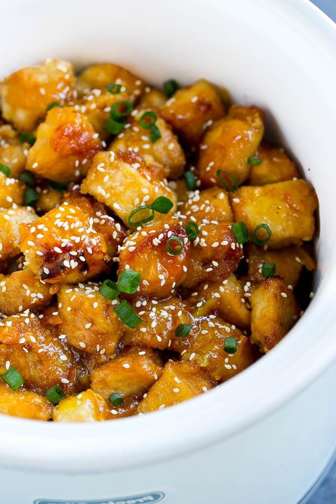Orangen-Hähnchen aus dem Slow Cooker im Topf, garniert mit Sesamsamen und Frühlingszwiebeln.