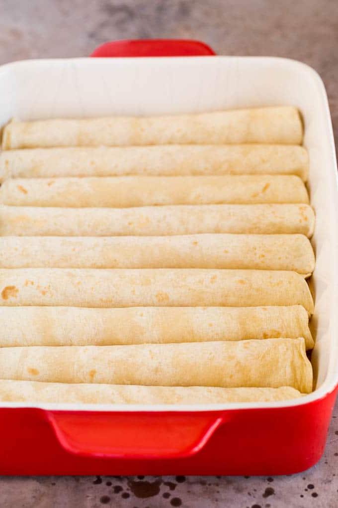 Gerollter Käse in Tortillas, dicht gepackt in einer Auflaufform, bereit zum Übergießen mit Soße.