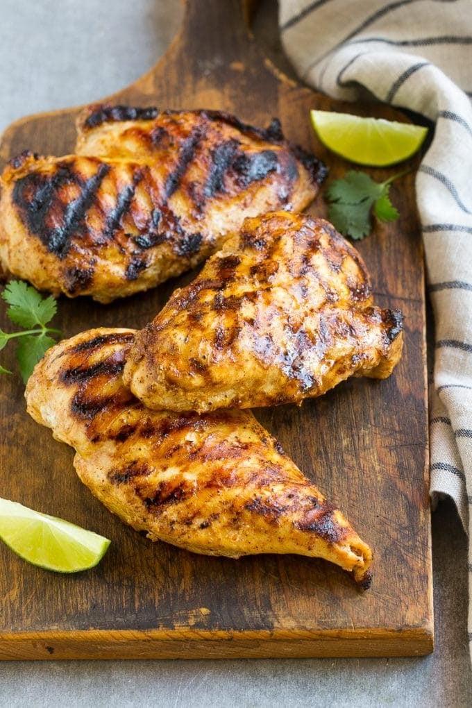 Gegrillte Hähnchenbrüste auf einem Holzschneidebrett, bereit zum Schneiden.