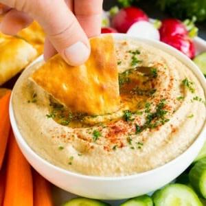 Eine Hand taucht Pitabrot in Baba Ganoush.