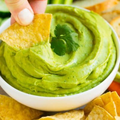 Ein Tortilla-Chip schöpft eine Portion Avocado-Dip auf.