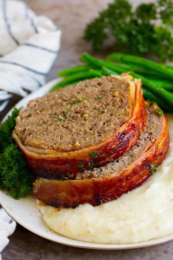 Hackbraten im Speckmantel Rezept | Rinderhackbraten #hackbraten #rindfleisch #rinderhack #speck #abendessen #abendessenimzoo Scheiben von in Speck gewickeltem Hackbraten, serviert über Kartoffelpüree mit grünen Bohnen.