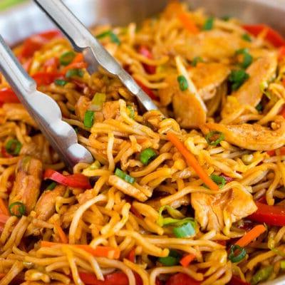 Yakisoba Nudeln mit Hähnchen 2 Tongs serving up a portion of yakisoba noodles with vegetables and chicken.
