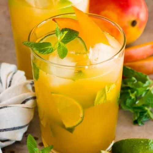 Mango Mojito 7 Gläser mit Mango Mojito, garniert mit frischer Minze, Limetten und Mangoscheiben. Nahaufnahme des fertigen Cocktails.