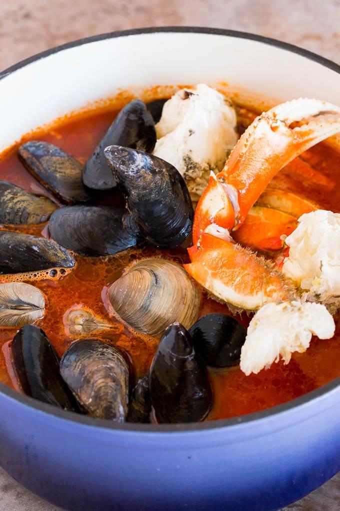 Krabben, Miesmuscheln und Venusmuscheln in einem großen Topf mit reicher, roter Tomatenbrühe, die sanft für Cioppino köchelt und ihre Aromen abgibt.