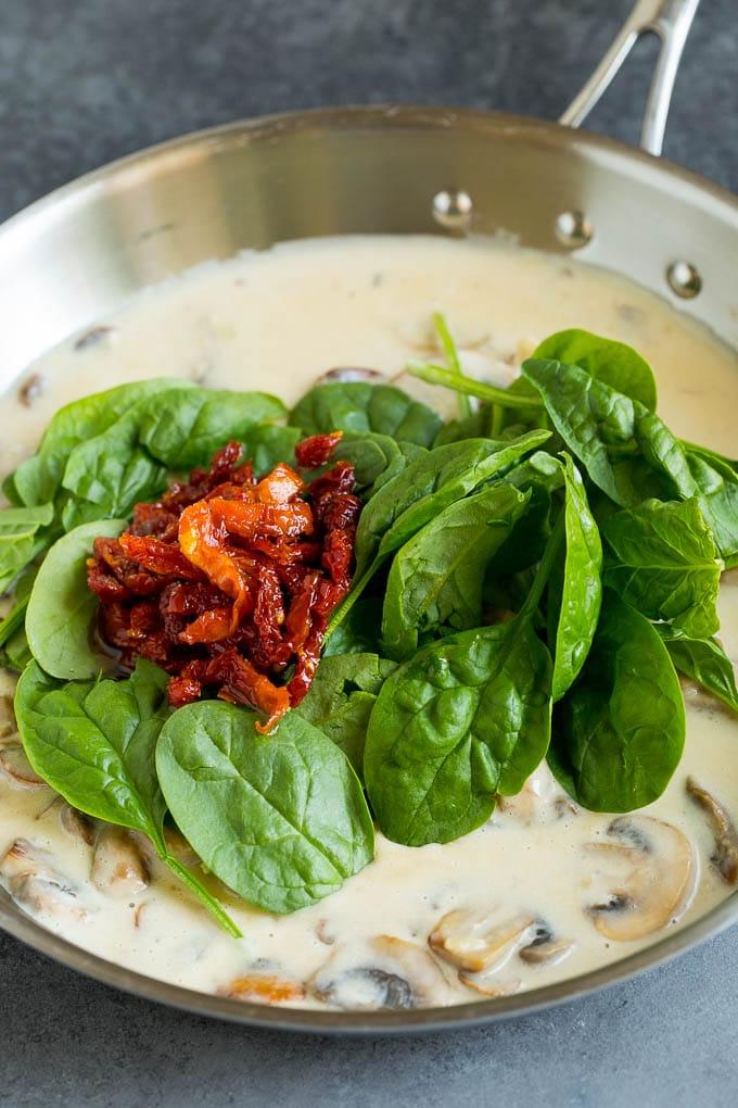 Eine Pfanne mit cremiger Pilzsoße mit Spinat und sonnengetrockneten Tomaten.