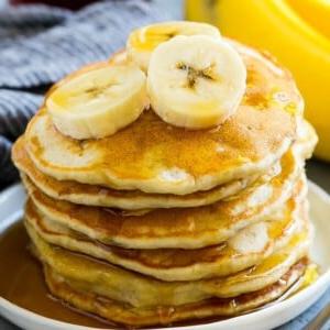 Ein Stapel Bananenpfannkuchen mit Bananenscheiben und Ahornsirup.