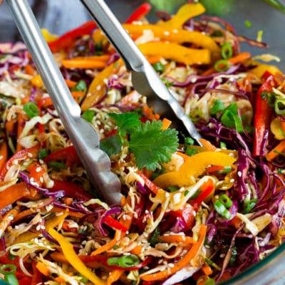Asiatischer Krautsalat mit Sesamdressing 2 Zange, die eine Portion asiatischen Krautsalats serviert.