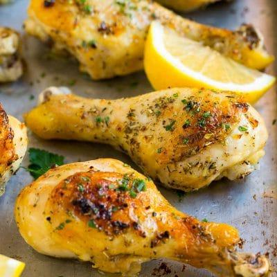 Hähnchenunterkeulen aus dem Ofen mit Knoblauch und Kräutern 2 Gebackene Hähnchenschenkel mit Knoblauch und Kräutern, garniert mit Zitronenspalten und Petersilie.