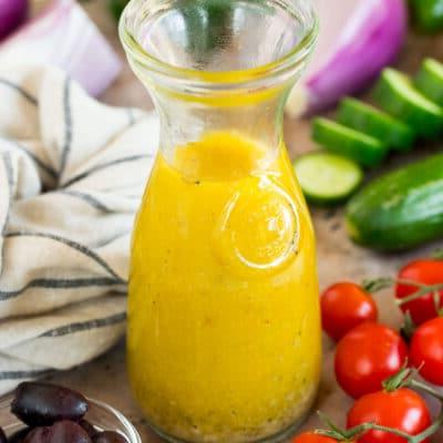 Griechisches Salatdressing 7 Eine Flasche griechisches Salatdressing umgeben von frischem Gemüse.