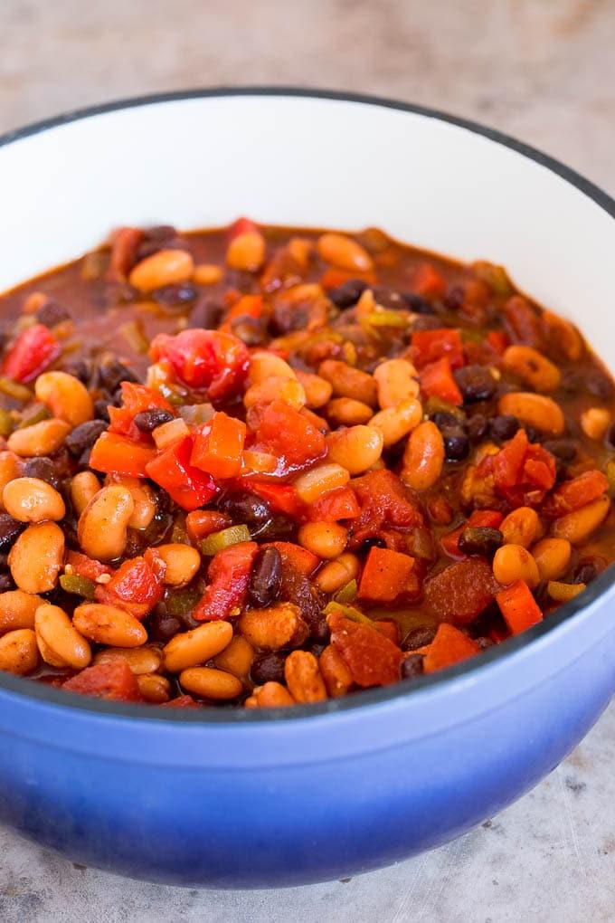 Eine Nahaufnahme von Bohnen, Paprika, Zwiebeln und Tomaten in einem großen Suppentopf, die darauf warten, gekocht zu werden.