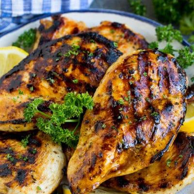 Die beste Hähnchenmarinade, die gegrillte Hähnchenbrüste bedeckt und mit Zitrone garniert ist.
