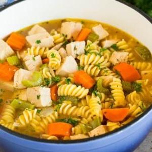 Ein Topf Putennudelsuppe mit Gemüse, garniert mit Petersilie.