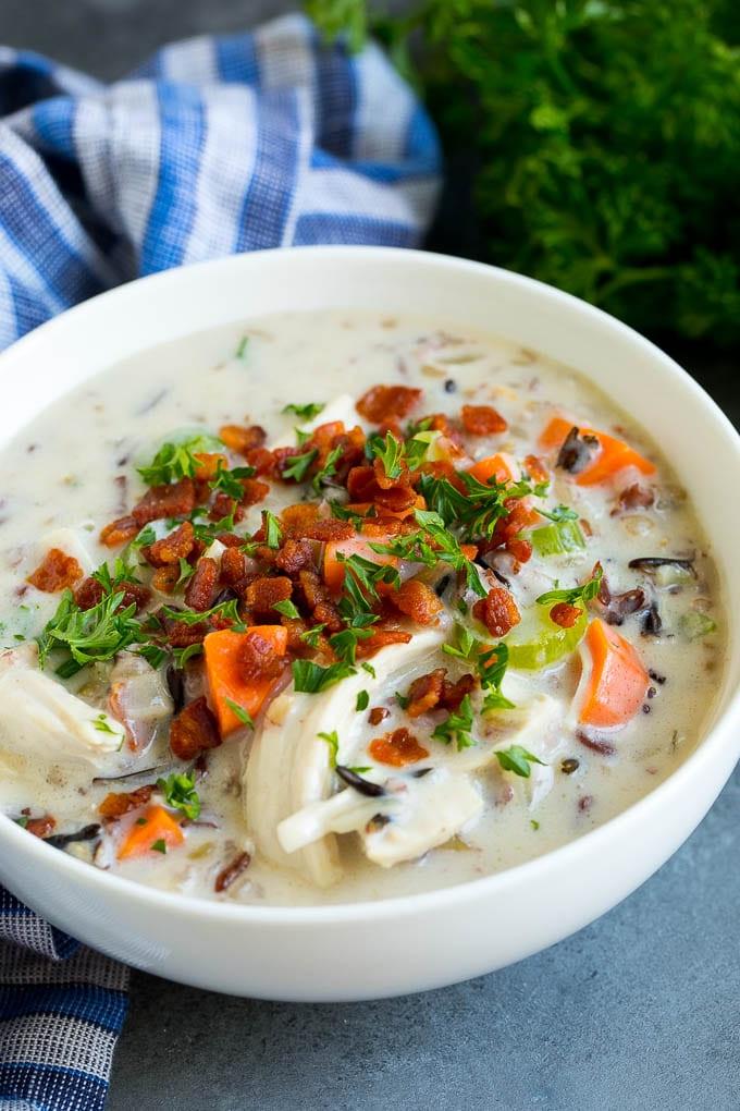 Eine Schüssel Hähnchen-Wildreis-Suppe, garniert mit Speck und Petersilie.