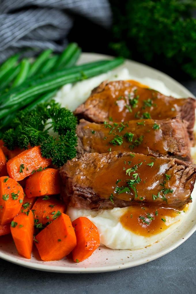 Slow Cooker Rinderbrust serviert über Kartoffelpüree mit Gemüse als Beilage.