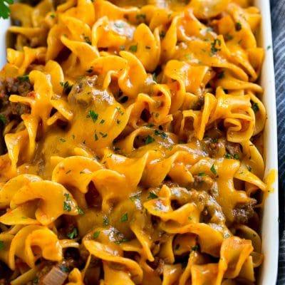 Rindfleisch-Nudelauflauf 2 Hackfleisch-Nudel-Auflauf in einer Servierschale mit geschmolzenem Cheddar-Käse und Petersilie garniert.