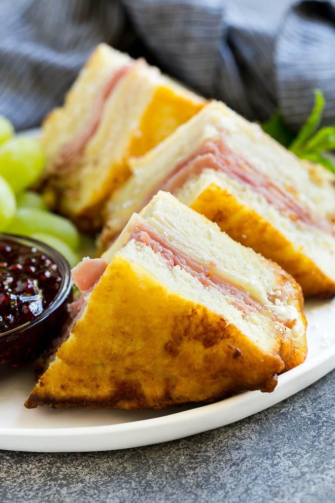 Viertel von Monte Cristo Sandwiches, bestreut mit Puderzucker und serviert mit Himbeermarmelade und frischem Obst.
