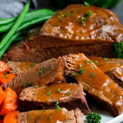 Slow Cooker Rinderbrust 2 Aufgeschnittene Slow Cooker Rinderbrust mit Sauce und Gemüse serviert.
