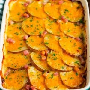 18 Schinkenreste-Rezepte 9 Eine Auflaufform mit Kartoffelgratin und Schinken, belegt mit geschmolzenem Käse und Petersilie.