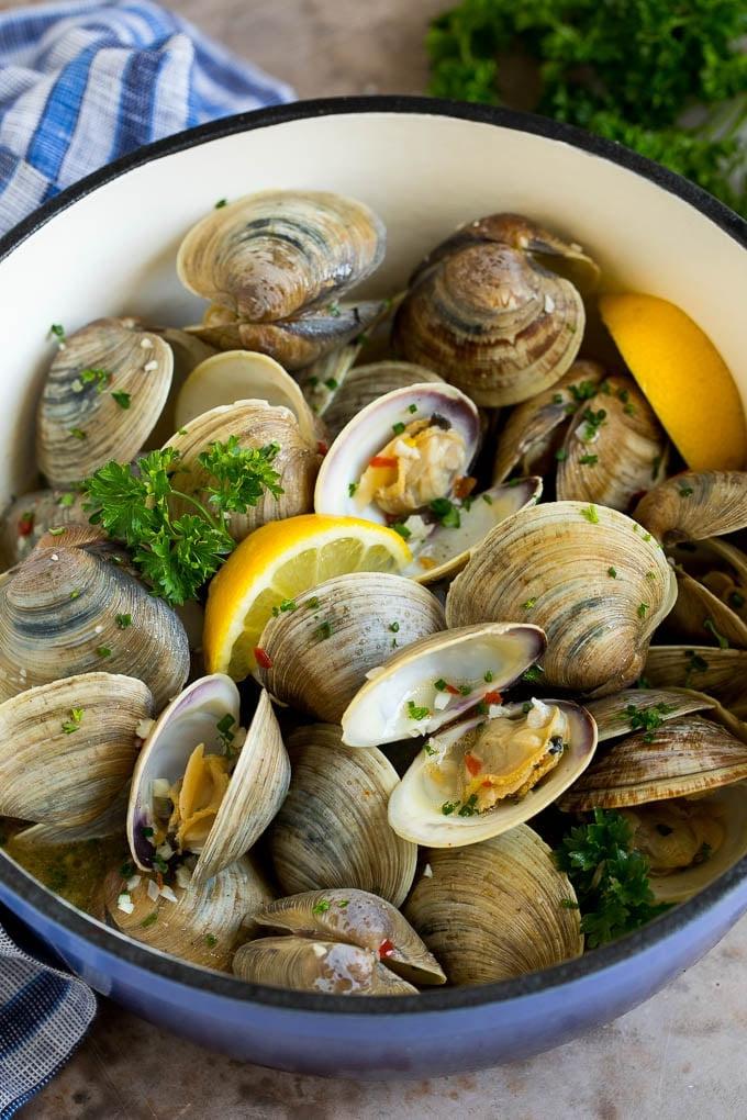 Ein Topf mit gedämpften Muscheln, Zitronenspalten und Petersilie garniert.