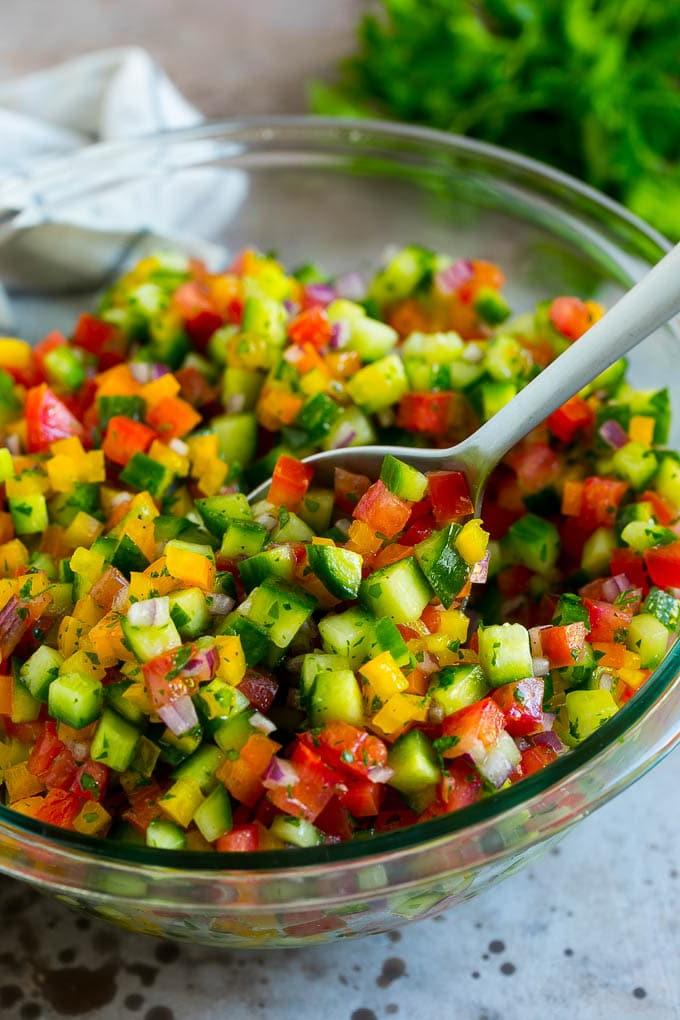 Israelischer Salat Rezept | Gurken-Salat | Tomaten-Salat | Gehackter Salat #salad #cleaneating #healthy #glutenfree #lowcarb #keto #sidedish #lunch #ahurt Eine Schüssel Israelischer Salat mit einem Servierlöffel darin.