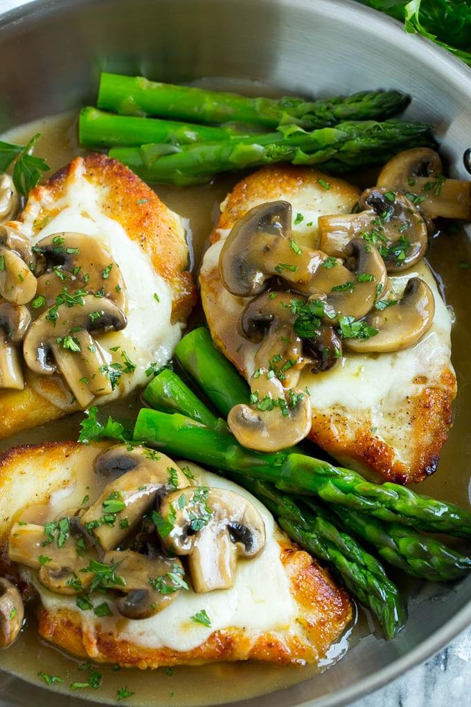 Gekochtes Hähnchen Madeira in einer Edelstahlpfanne, bedeckt mit geschmolzenem Käse und Pilzsauce.
