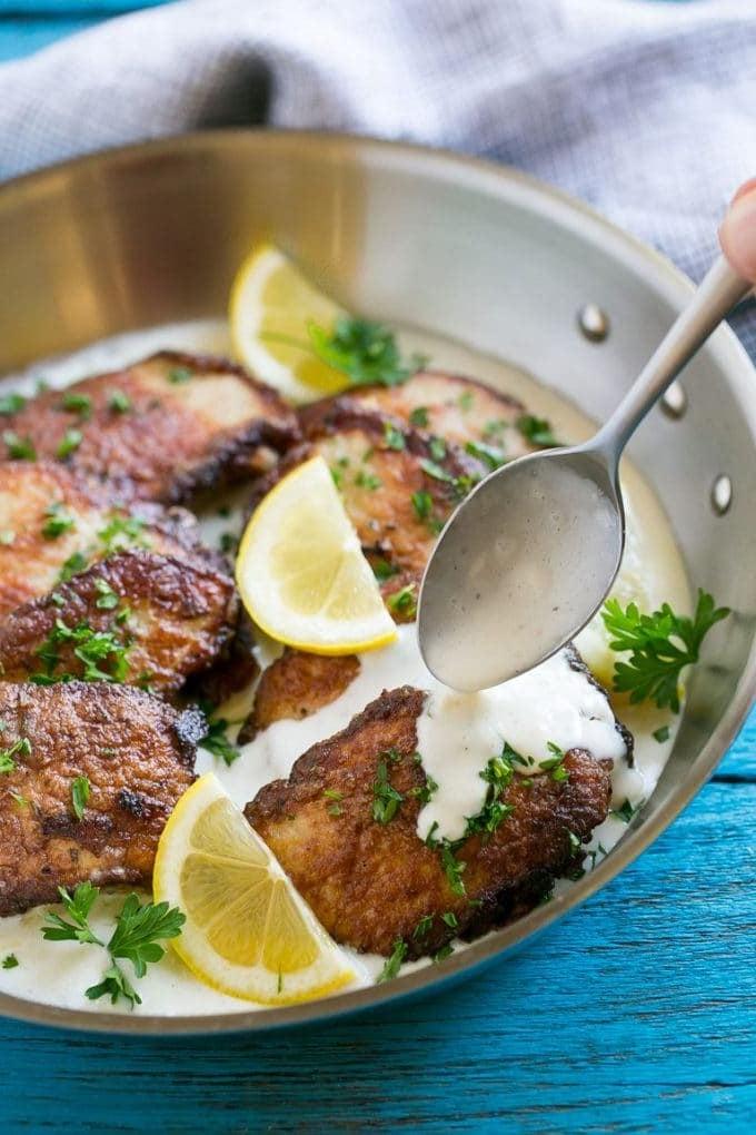 Schweine-Scallopini in einer Pfanne mit einem Löffel, der cremige Soße darüber träufelt.