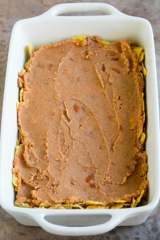 Eine Schicht Bohnenmus auf den zerstoßenen Tortilla Chips in einer Auflaufform.