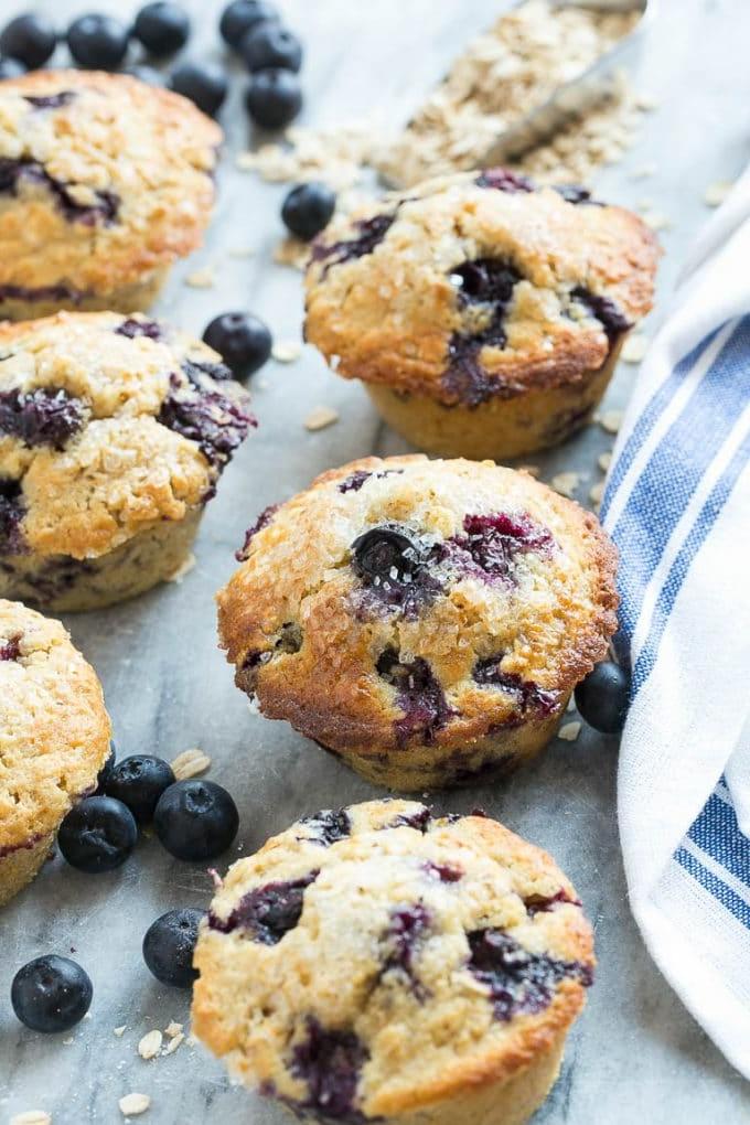 Mehrere gesunde Blaubeermuffins auf einer Marmorplatte mit frischen Blaubeeren.