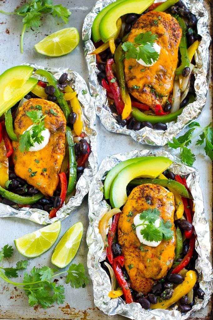 Eine Auswahl an vorbereiteten Fajita-Hähnchen-Alupäckchen auf einem Backblech, bereit zum Kochen.