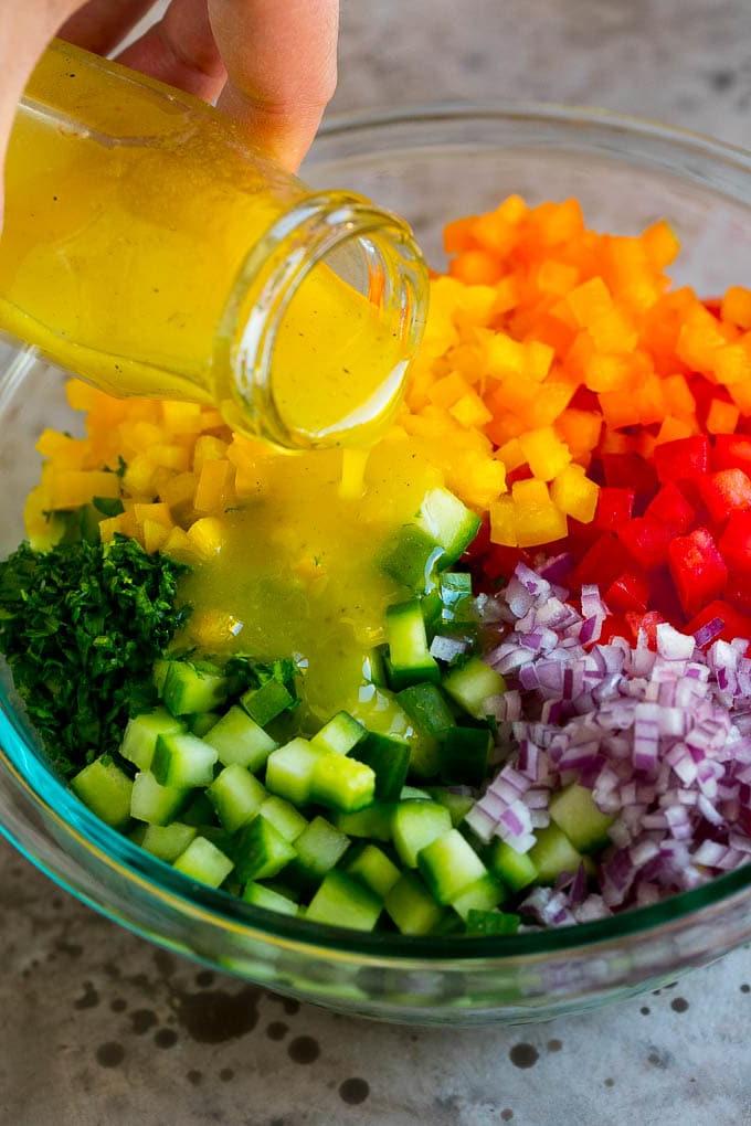 Israelischer Salat Rezept | Gurken-Salat | Tomaten-Salat | Gehackter Salat #salad #cleaneating #healthy #glutenfree #lowcarb #keto #sidedish #lunch #ahurt Zitronendressing wird über gehacktes Gemüse gegossen.