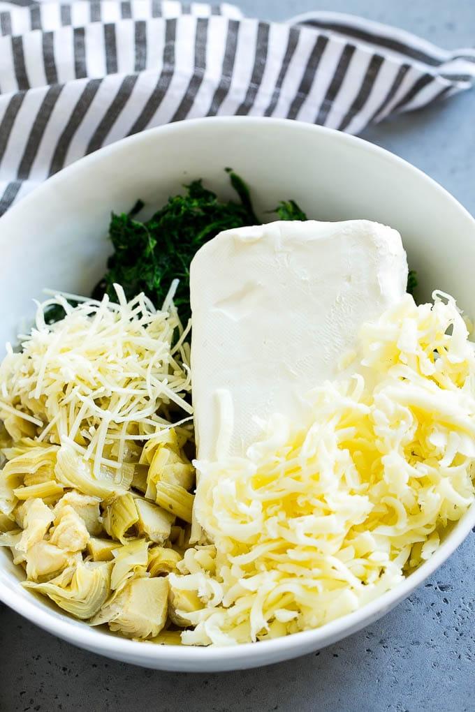 Frischkäse, Spinat, Artischocken und geriebener Käse in einer Schüssel.