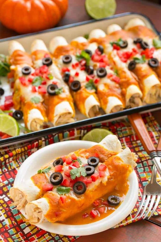 Kürbis-Enchiladas 5 Kürbis-Enchiladas auf einem kleinen Teller mit einem Blech Enchiladas dahinter.