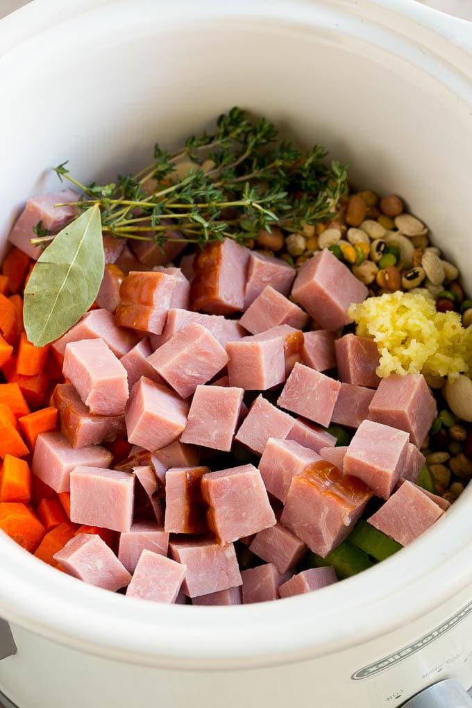 Schinken-Bohnen-Suppen-Rezept | Slow Cooker Schinken-Bohnen-Suppe | Crockpot Schinken-Bohnen-Suppe | Rezept für Schinkenreste #schinken #bohnen #suppe #slowcooker #crockpot #abendessen #abendessenimzoo Gemüse, Schweinefleisch, Kräuter und Knoblauch im Slow Cooker.