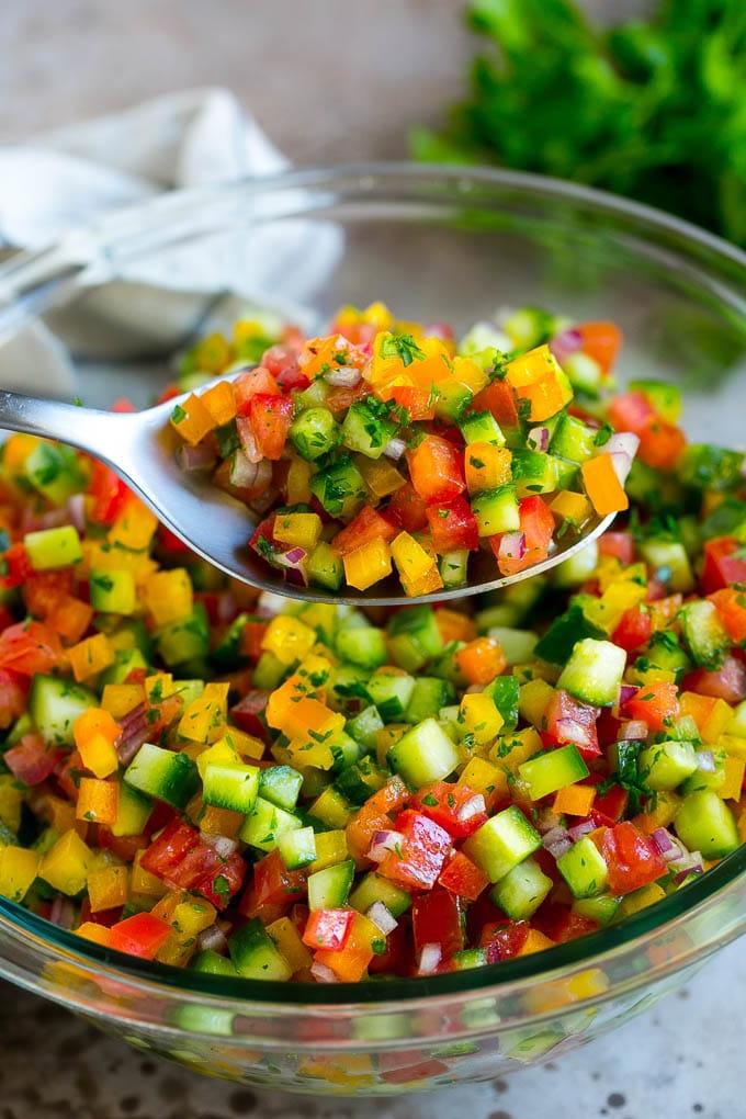 Israelischer Salat Rezept | Gurken-Salat | Tomaten-Salat | Gehackter Salat #salad #cleaneating #healthy #glutenfree #lowcarb #keto #sidedish #lunch #ahurt Ein Löffel hält eine Portion Israelischen Salat hoch.