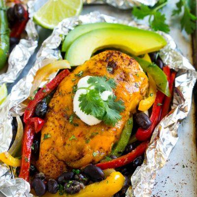 Hähnchen-Fajita-Folienpäckchen 2 Gegarte Hähnchenbrust mit Käse, umgeben von Paprika, Zwiebeln und schwarzen Bohnen in einer geöffneten Alufolie.