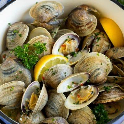 Ein Topf mit gedämpften Muscheln, Zitronenspalten und Petersilie garniert.