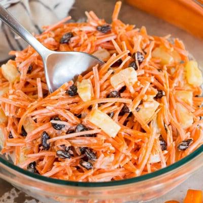 Karottensalat 7 Eine Schüssel cremiger Karottensalat mit einem großen Löffel darin.
