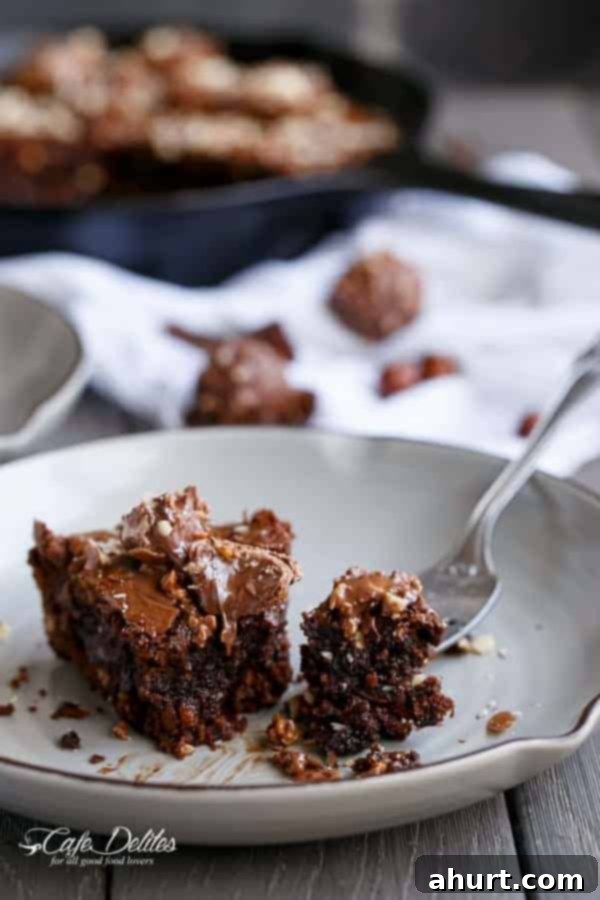 Ultimate Ferrero Rocher Skillet Brookie 11 A close-up of a fork holding a bite of Ferrero Rocher Deep Dish Skillet Brownie Cookie, showing its fudgy texture and hazelnut bits.