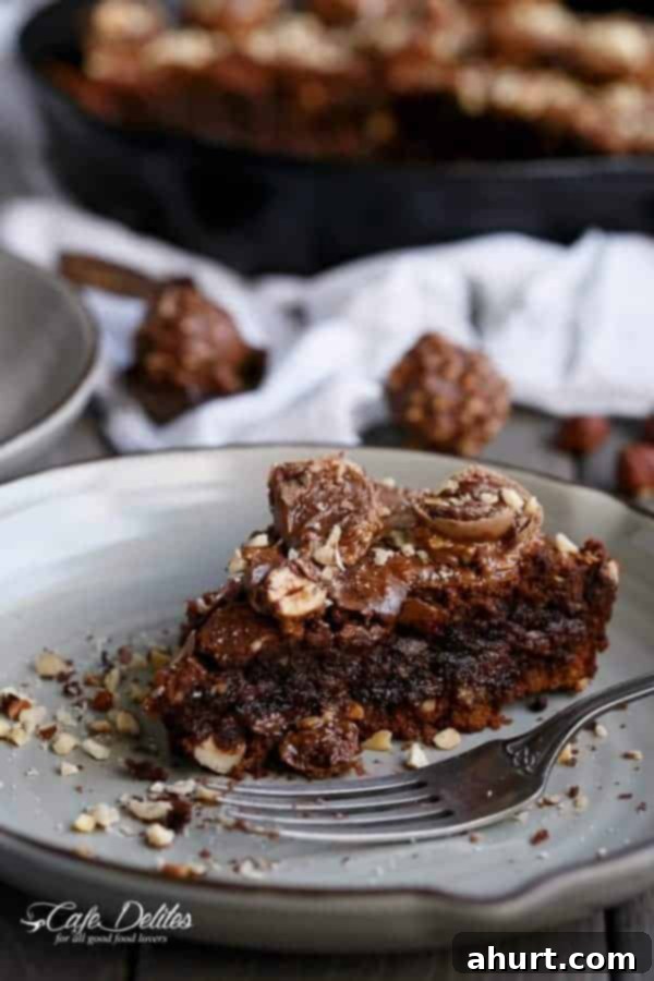 Ultimate Ferrero Rocher Skillet Brookie 5 A close-up of a warm Ferrero Rocher Deep Dish Skillet Brownie Cookie, glistening with melted chocolate and topped with hazelnuts.
