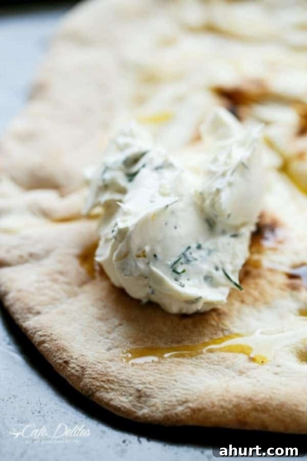 Creamy avocado spread being applied evenly over a pizza dough base, showing the preparation of the herb cream cheese layer.