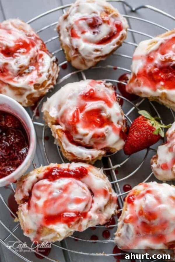 No Yeast Strawberries And Cream Cinnamon Rolls on a cooling rack, some with extra strawberry drizzle