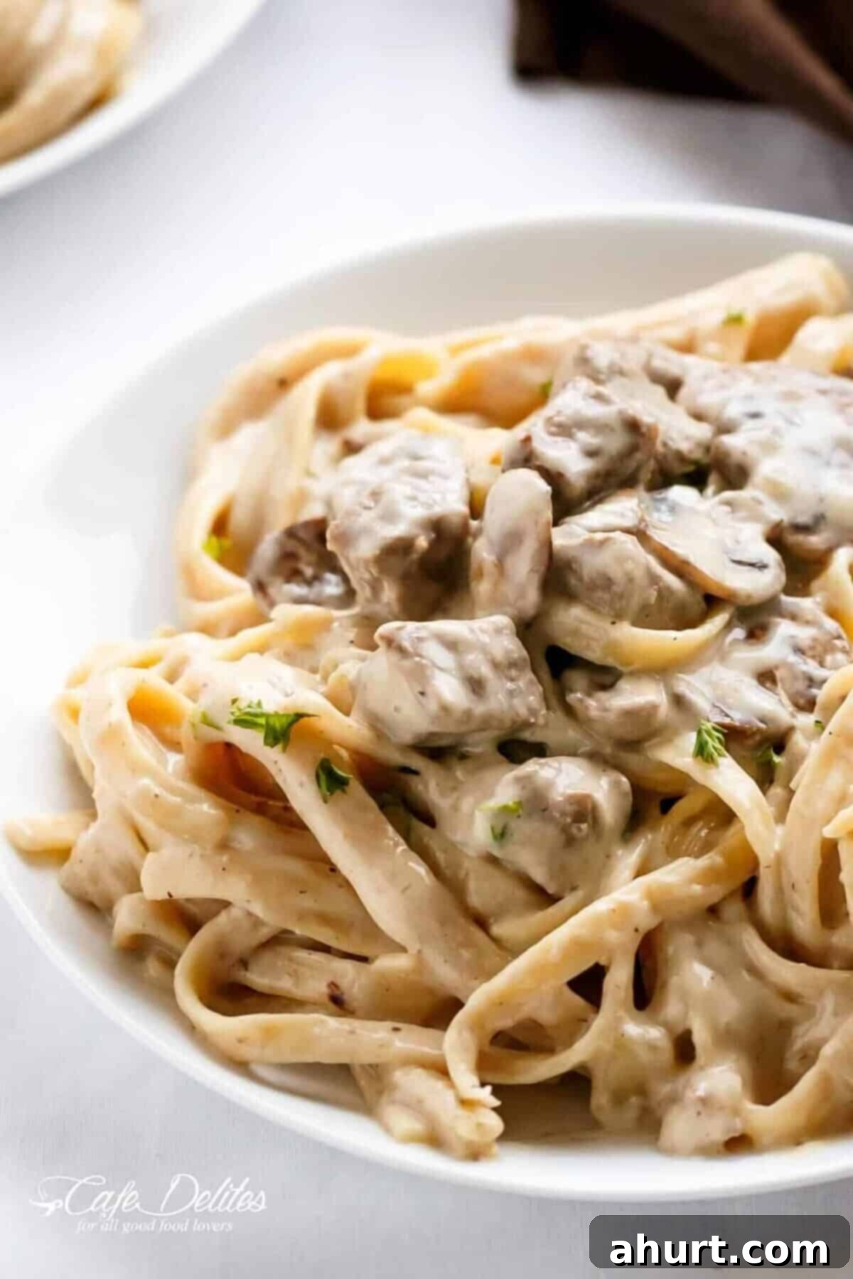 Velvety Beef Stroganoff with Earthy Mushrooms 2 A white round bowl filled with creamy beef stroganoff, featuring tender, chunky steak bites, served over pasta in a rich, velvety sauce, garnished with fresh parsley.