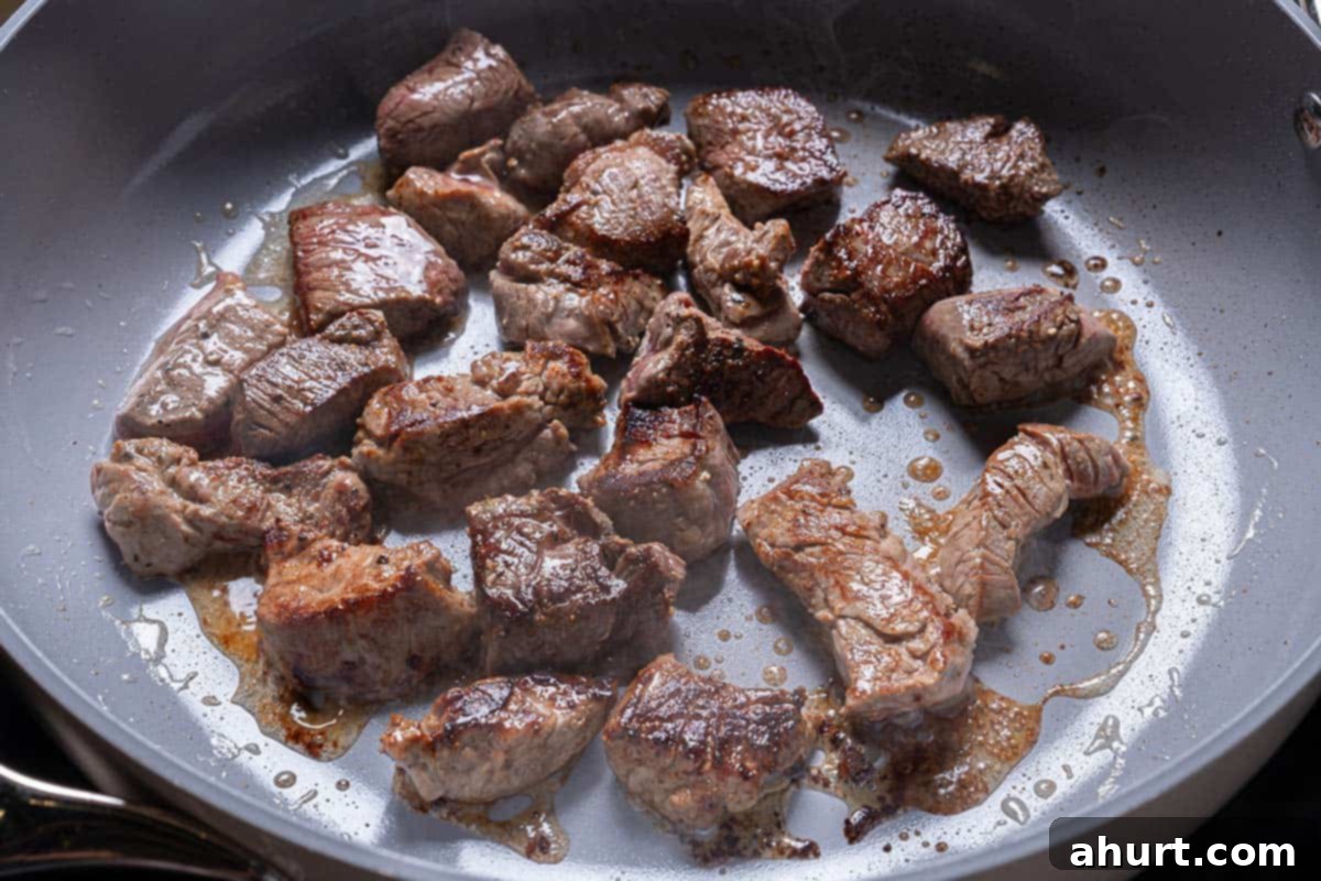 Velvety Beef Stroganoff with Earthy Mushrooms 5 Steak Chunks being seared in a large pan over medium heat, achieving a golden brown crust.