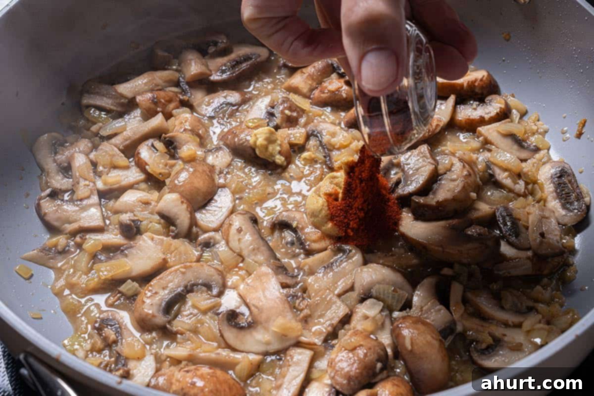 Velvety Beef Stroganoff with Earthy Mushrooms 6 Sliced mushrooms, chopped onions, and minced garlic being cooked in the same pan where steak chunks were previously seared, caramelizing in the residual butter.