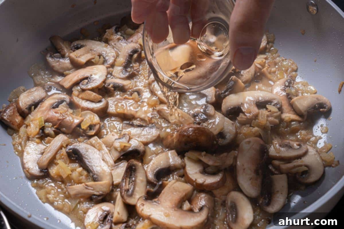 Velvety Beef Stroganoff with Earthy Mushrooms 7 Dry white wine being poured into the pan with cooked vegetables, creating steam as it deglazes the pan.