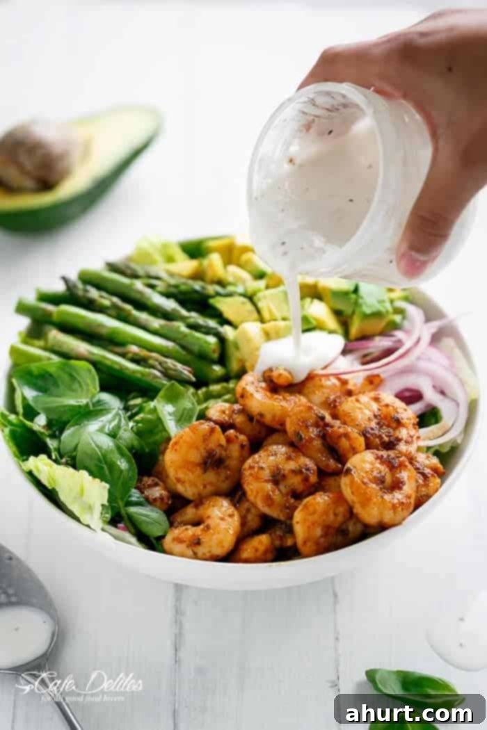 Seared Blackened Shrimp & Vibrant Green Salad 4 Creamy Lemon Pepper Yogurt Dressing being poured generously over the Blackened Shrimp, Asparagus and Avocado Salad, adding a luscious finish.