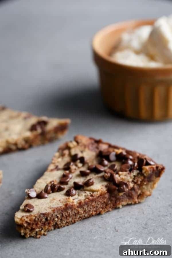 A perfectly baked slice of Low Carb Browned Butter Chocolate Chip Skillet Cookie, showcasing its fudgy center and chocolate chips, served from a cast iron skillet.