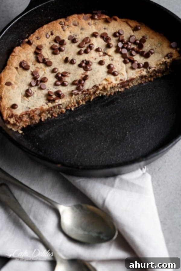 A golden-brown Low Carb Browned Butter Chocolate Chip Skillet Cookie, perfectly half-eaten in its cast iron pan, showing a soft interior.